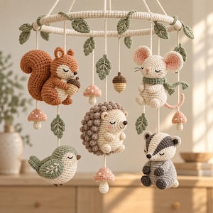 May include: A crochet mobile featuring a circular frame adorned with green leaves. Hanging from the frame are five stuffed animals: a squirrel with an acorn, a mouse with a scarf, a hedgehog, a bird, and a badger, interspersed with small mushrooms.