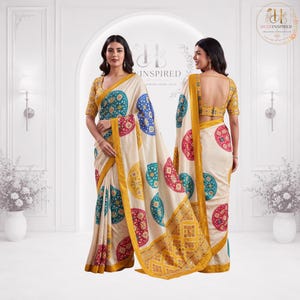 May include: A cream-coloured saree featuring a repeating pattern of circular motifs in red, yellow, and teal. The garment includes a matching mustard yellow blouse with short sleeves and a wide border, showcasing a traditional design with intricate details.