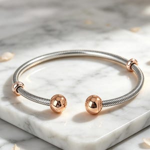 May include: A silver-toned snake chain bracelet featuring a flexible, textured band. The bracelet is accented with two polished rose gold-toned spherical end caps and two smaller rose gold-toned sliding beads positioned along the chain.