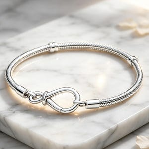 May include: A silver snake chain bracelet featuring a polished infinity-shaped clasp. The bracelet has a flexible, textured metal band with two fixed silver stations positioned along the chain, creating a sleek and continuous circular design.