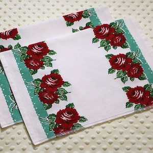May include: Two white tea towels with a green and white border and red rose pattern.