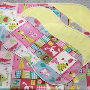 May include: A set of baby items, including a pink and white patterned blanket with animal and letter designs, and two yellow absorbent pads. The patterned pad has a patchwork design with animals and letters.