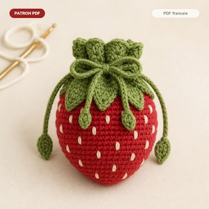 May include: A handmade crochet strawberry-shaped pouch. The pouch is primarily red with white seed details, green leaves, and a drawstring closure. The text "PATRON PDF" is in the upper left corner.