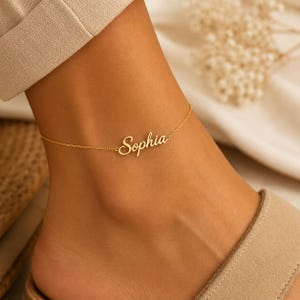 May include: A gold-toned anklet featuring a delicate chain and a central nameplate pendant with the name Sophia written in a cursive script font. The jewellery piece is secured around the ankle with a thin, polished metal link chain design.