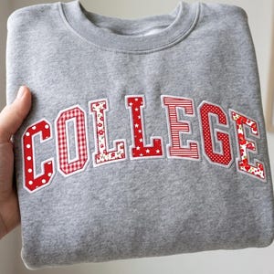 Puede incluir: Una sudadera gris jaspeado de cuello redondo con la palabra COLLEGE aplicada en el pecho en letras de bloque. Cada letra está confeccionada con tela roja y blanca con varios patrones, incluyendo lunares, cuadros vichy, rayas y flores.