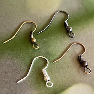May include: Close-up of four different metal earring hooks. The hooks are in gold, silver, gunmetal, and copper colors. Each hook has a coiled spring and a small loop for attaching earrings.