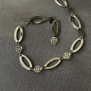 May include: A silver chain necklace with oval links and decorative flower accents.