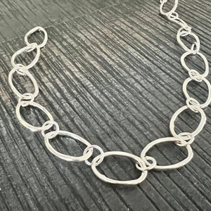 May include: A silver chain with oval links. The chain is laid out on a dark wood surface.