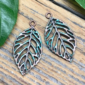 May include: Two copper leaf charms with a turquoise patina. The leaves are cut out and have a delicate design. The charms have a loop at the top for attaching to jewelry or other crafts.