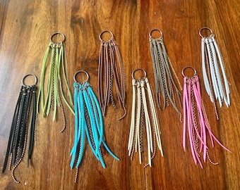 May include: Assortment of ten colourful tassel keychains with gold chain accents. Each keychain features a silver ring with multiple strands of leather tassels and a gold chain with small beads.