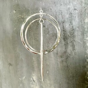 Puede incluir: Pendientes de aro de plata con dos c&iacute;rculos superpuestos y una varilla larga, delgada y puntiaguda de plata que cuelga de la parte inferior.