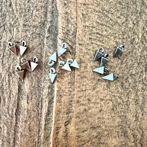 May include: A collection of small triangle-shaped metal charms with a loop at the top. The charms are in two colors: gold and silver.