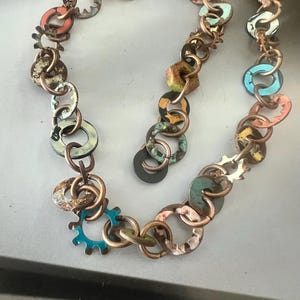 May include: A necklace made of copper chain links and colorful metal washers. The washers are painted in various shades of blue, green, orange, and brown. The necklace has a rustic, industrial look.