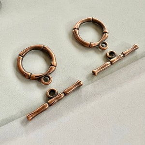 May include: Two copper-toned metal toggle clasps with a bamboo-like design. Each clasp has a round ring and a bar with a loop at each end.