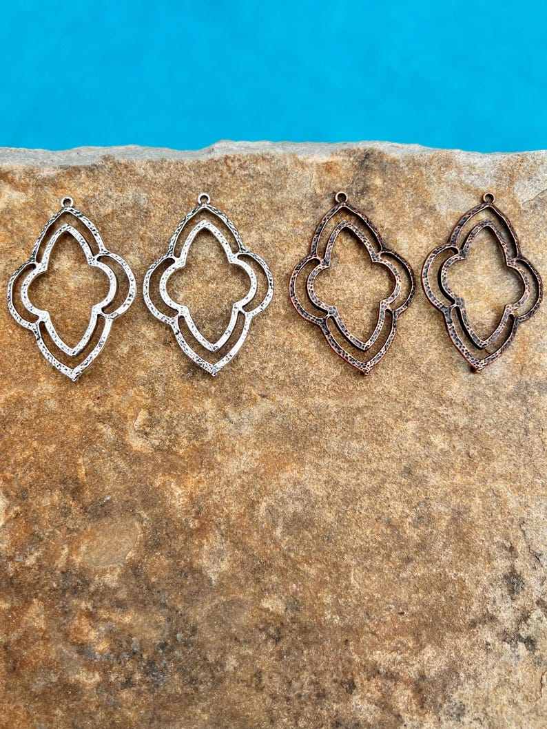 May include: Four metal pendant charms in the shape of a quatrefoil. Two charms are silver and two are copper.