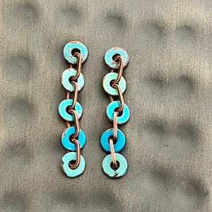 May include: A pair of long, dangling earrings with a graduated chain of turquoise blue and copper colored circles.