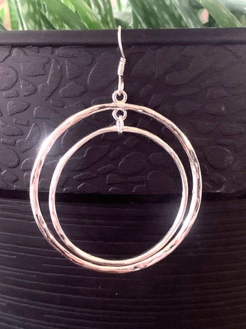 Puede incluir: Pendientes de aro de plata con un dise&ntilde;o de doble c&iacute;rculo. Los pendientes tienen una textura martillada y un estilo simple y elegante.