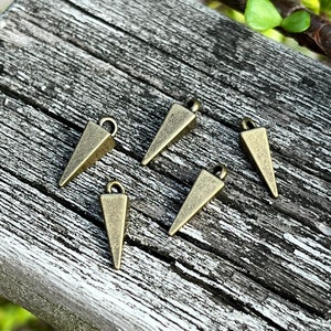 May include: Five gold-toned triangle-shaped metal charms with a loop at the top. The charms are arranged on a wooden surface.