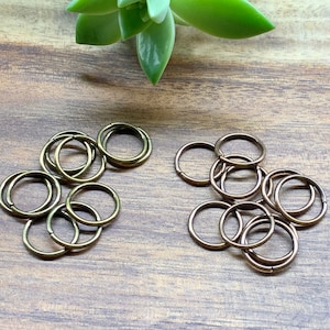 May include: A collection of 18 gold-toned metal jump rings. The rings are arranged in two groups on a wooden surface.