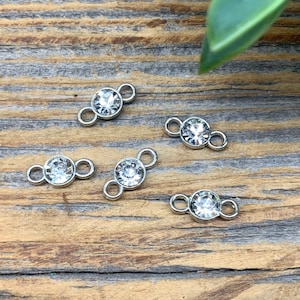 May include: Five silver-toned connector charms with clear crystal rhinestones. Each charm has two loops for attaching to jewelry.