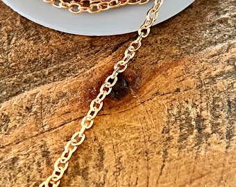 May include: A spool of gold-colored chain, with a length of chain extending from the spool. The chain is on a wooden surface.