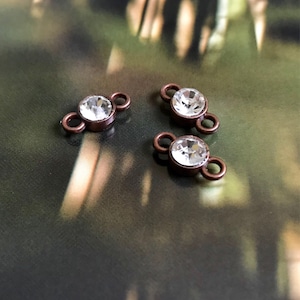 May include: Three copper-toned metal connector charms with clear crystal rhinestones. Each charm has two loops for attaching to jewelry.