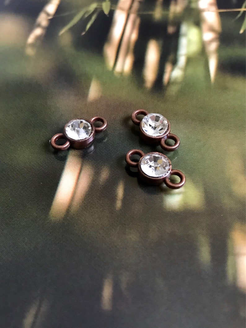 May include: Three copper-toned metal connector charms with clear crystal rhinestones. Each charm has two loops for attaching to jewelry.