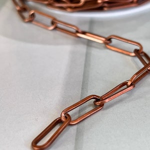May include: A close-up of a copper chain with oval links. The chain is lying on a white surface.