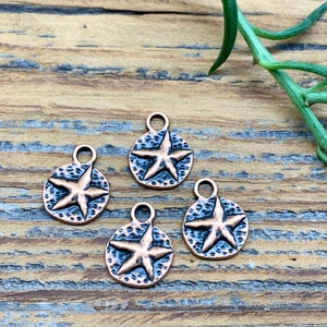 May include: Four copper-toned metal charms in the shape of a circle with a five-pointed star in the center. The charms have a textured surface and are perfect for jewelry making.