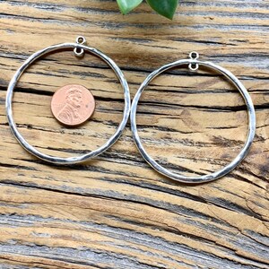 Puede incluir: Dos pendientes de aro de plata con acabado martillado. Los aros son grandes y tienen un di&aacute;metro de unos 5 cm. Los pendientes se muestran sobre una superficie de madera.