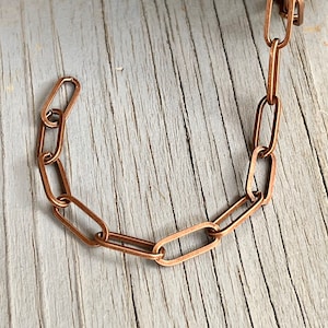 May include: A close-up of a copper chain with oval links. The chain is lying on a wooden surface.