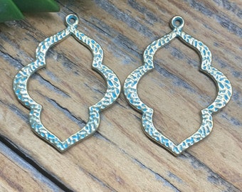 Puede incluir: Dos colgantes calados de metal con forma de cuadrifolio, perfectos para la creación de joyas. Los colgantes tienen un acabado dorado antiguo texturizado con un lavado azul turquesa. Cada colgante tiene un pequeño lazo en la parte superior.