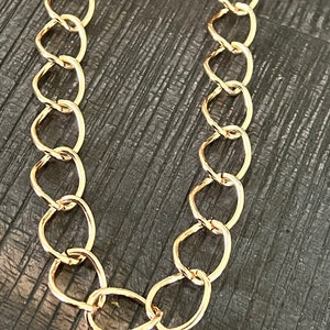 May include: A gold chain necklace with oval-shaped links. The chain is on a dark brown surface.