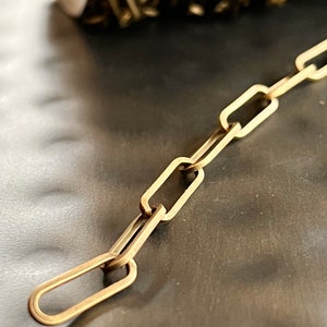 May include: A gold chain made of linked oval-shaped pieces. The chain is lying on a dark gray surface.
