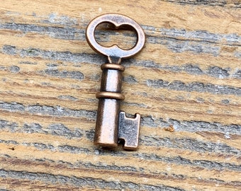 May include: A small, antique-looking key made of copper metal. The key has a simple design with a rounded head and a straight shaft. The key is lying on a wooden surface.