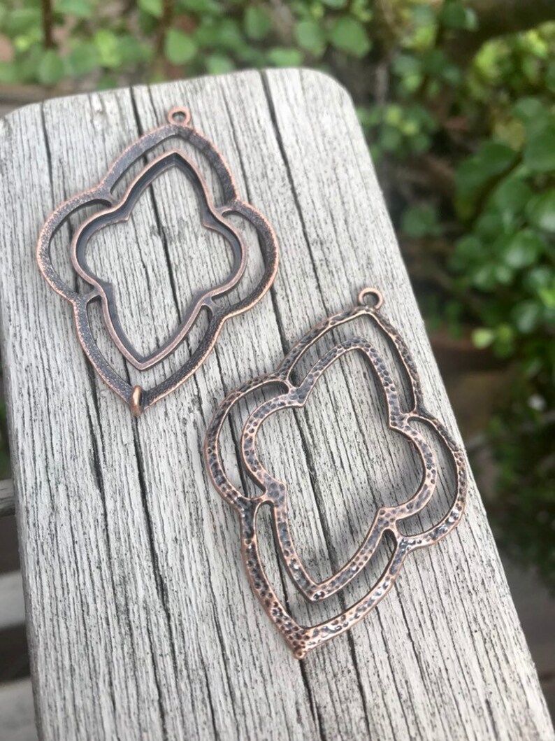 May include: Two antique copper-colored metal pendant charms shaped like a stylized flower with a double-layered design.