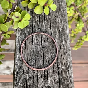 May include: A simple copper bangle bracelet, lying on a wooden surface.