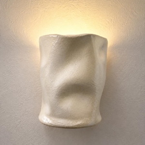 May include: A wall-mounted light fitting with an off-white, textured, and irregularly shaped ceramic shade. The surface features organic, undulating curves and indentations, emitting a soft, warm glow from the top and bottom edges.