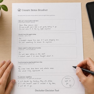Può includere: Un foglio di carta bianco intitolato Unsure Items Resolver con il piè di pagina Declutter Decision Tool. Il documento contiene cinque sezioni con risposte scritte a mano su un vaso in ceramica blu e un cerchio di decisione finale Let it go.