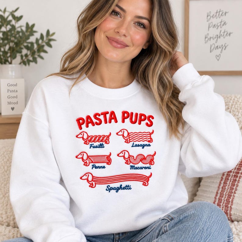 May include: A white crewneck sweatshirt featuring a red graphic print with the text PASTA PUPS. The design displays five dachshund dogs illustrated as different pasta shapes labeled Fusilli, Lasagna, Penne, Macaroni, and Spaghetti in blue.