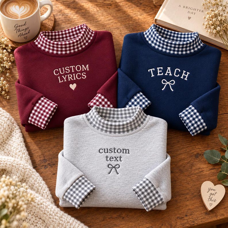 May include: Three long-sleeve sweatshirts in maroon, navy blue, and heather gray. Each features a mock neck and sleeve cuffs with a gingham pattern. The maroon shirt says CUSTOM LYRICS with a heart, navy says TEACH with a bow, and gray says custom text with a bow.