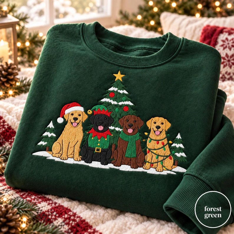 May include: A forest green crewneck sweatshirt featuring an embroidered design of four dogs sitting in front of a Christmas tree. The dogs include a golden retriever in a Santa hat, a black dog in an elf costume, a brown dog with a green scarf, and a golden retriever wrapped in colorful string lights.