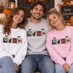 May include: Three crewneck sweatshirts in white, light gray, and light pink, each featuring a horizontal row of four square postage-stamp style graphics depicting a witch on a broom, a black cat, a jack-o'-lantern, and the text BOO.