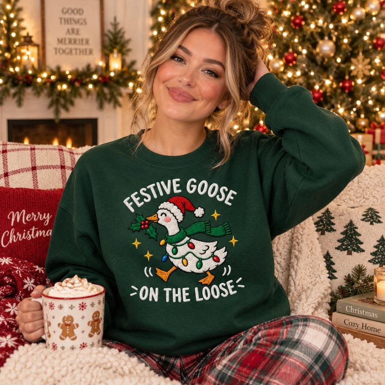 May include: A dark green crewneck sweatshirt featuring a graphic of a white goose wearing a red Santa hat and a green scarf. The goose is wrapped in colorful Christmas lights and holds a sprig of holly. Text reads: FESTIVE GOOSE ON THE LOOSE.