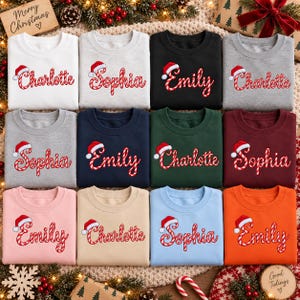 May include: A collection of twelve crewneck sweatshirts in various colors including white, gray, black, navy, dark green, maroon, pink, beige, light blue, and orange. Each sweatshirt features a name embroidered in a candy cane pattern.