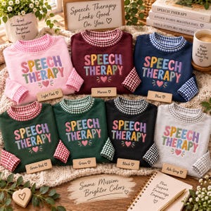 May include: Seven crewneck sweatshirts in light pink, maroon, blue, dark green, green, black, and ash gray. Each features the embroidered text SPEECH THERAPY in multicolored letters, a small heart, and a gingham-patterned collar and cuffs.