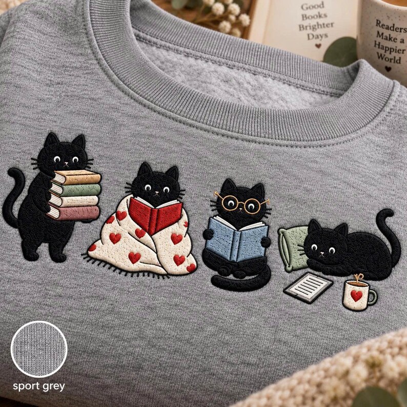 May include: A sport grey crewneck sweatshirt featuring an embroidered design of four black cats. One cat holds a stack of books, one is wrapped in a heart-patterned blanket reading, one wears glasses while reading, and one lies by a book and mug.