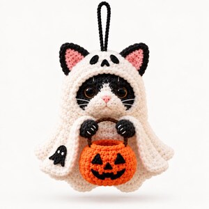 May include: A crocheted black and white cat ornament wearing a white ghost costume with a hood. The cat has large dark eyes, a pink nose, and holds a small orange crocheted pumpkin bucket with a black jack-o'-lantern face. A black loop is attached.