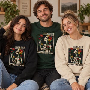 May include: Three crewneck sweatshirts in black, dark green, and beige, each featuring a graphic of a skeleton surrounded by red and yellow flowers. The text "EZEKIEL 37:1-10" and "DRY BONES COME TO LIFE" is printed above and below the illustration.