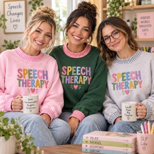 May include: Three sweatshirts featuring the embroidered text SPEECH THERAPY in colorful letters above a small heart. The pink sweatshirt has a pink gingham collar, the green has a pink gingham collar, and the gray has a gray gingham collar.